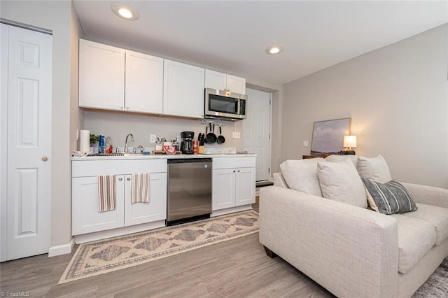 kitchen with appliances with stainless steel finishes, light wood finished floors, a sink, open floor plan, and white cabinetry