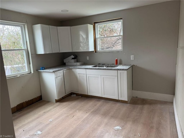 kitchen with light stone countertops, sink, white cabinets, and light hardwood / wood-style flooring