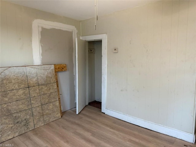 empty room with light wood-type flooring and wooden walls