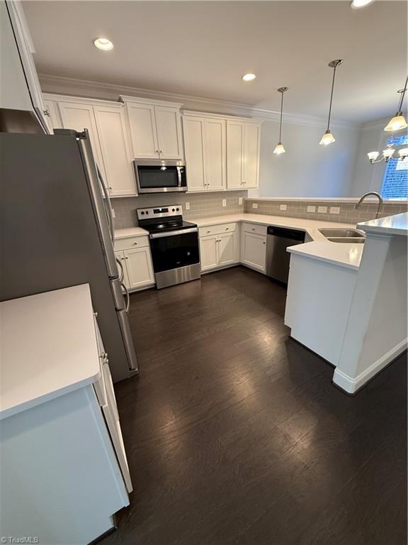 kitchen with sink, appliances with stainless steel finishes, white cabinetry, dark hardwood / wood-style flooring, and decorative light fixtures