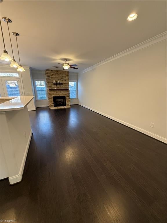 unfurnished living room with crown molding, dark hardwood / wood-style flooring, a wealth of natural light, ceiling fan, and a fireplace