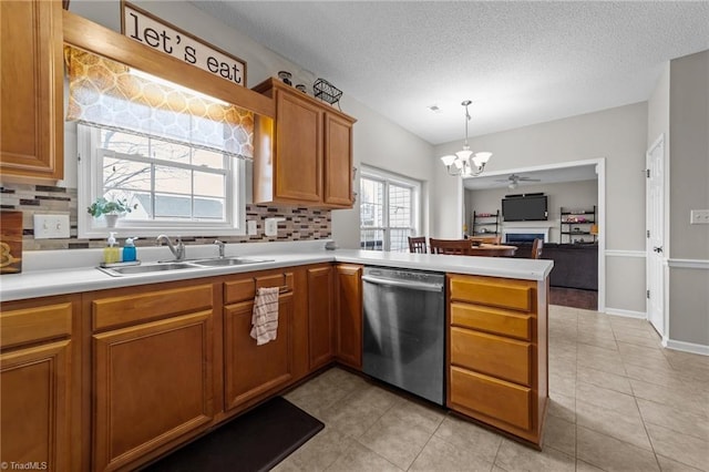 kitchen with brown cabinets, hanging light fixtures, light countertops, stainless steel dishwasher, and a sink