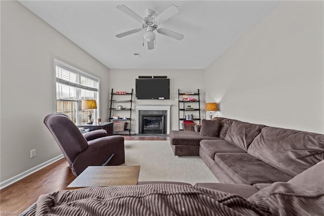 living room with dark wood-style flooring, a fireplace with flush hearth, a ceiling fan, and baseboards