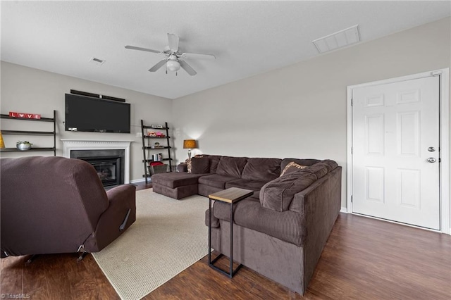 living room with a ceiling fan, visible vents, and dark wood finished floors