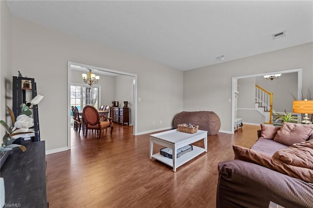 living area featuring baseboards, visible vents, dark wood finished floors, stairway, and an inviting chandelier