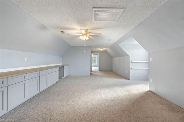 bonus room with light carpet, visible vents, ceiling fan, vaulted ceiling, and a textured ceiling