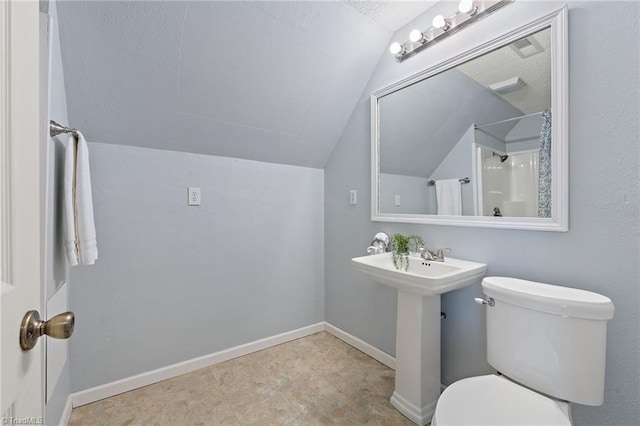 bathroom featuring lofted ceiling, toilet, a sink, baseboards, and walk in shower