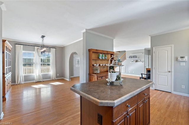 kitchen featuring a center island, pendant lighting, brown cabinets, arched walkways, and light wood-style floors