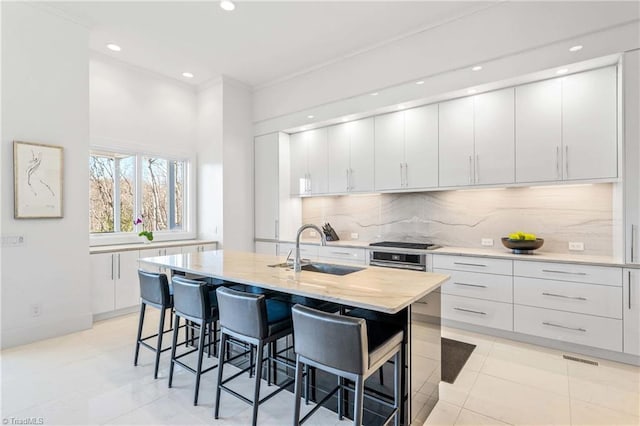 kitchen featuring appliances with stainless steel finishes, white cabinetry, an island with sink, sink, and a breakfast bar