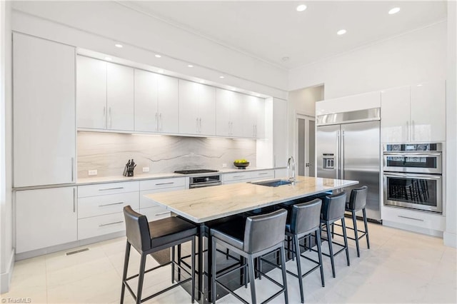 kitchen featuring white cabinetry, appliances with stainless steel finishes, a kitchen island with sink, a kitchen breakfast bar, and sink