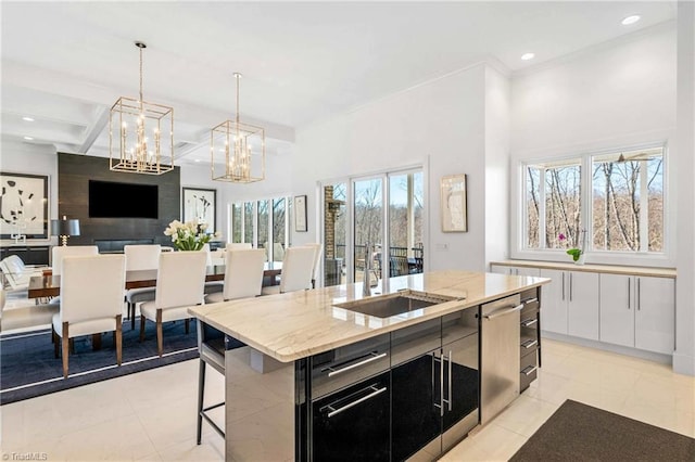 kitchen featuring dishwasher, beamed ceiling, sink, hanging light fixtures, and a center island with sink