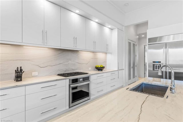 kitchen with appliances with stainless steel finishes, white cabinetry, decorative backsplash, sink, and light stone counters