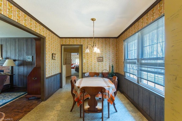 dining room featuring wallpapered walls, an inviting chandelier, wainscoting, ornamental molding, and a textured ceiling