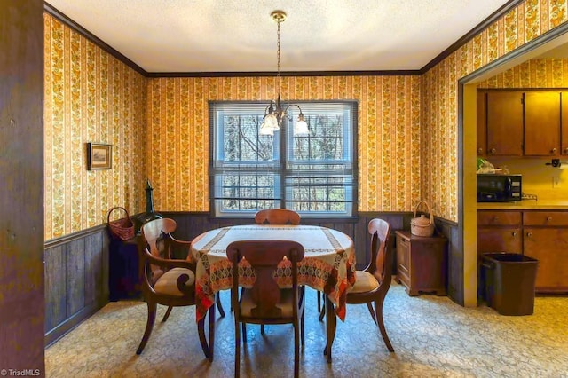 dining area featuring wainscoting, a textured ceiling, wallpapered walls, and ornamental molding