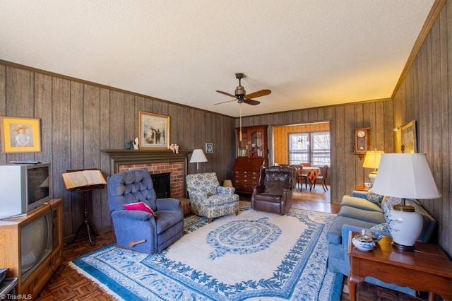 living room featuring ornamental molding, a textured ceiling, wood walls, a fireplace, and ceiling fan