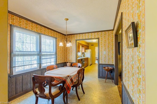 dining space with a wainscoted wall, a textured ceiling, ornamental molding, and wallpapered walls