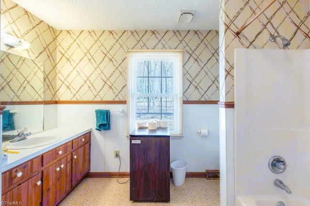 bathroom featuring a textured ceiling, wallpapered walls, vanity, and baseboards