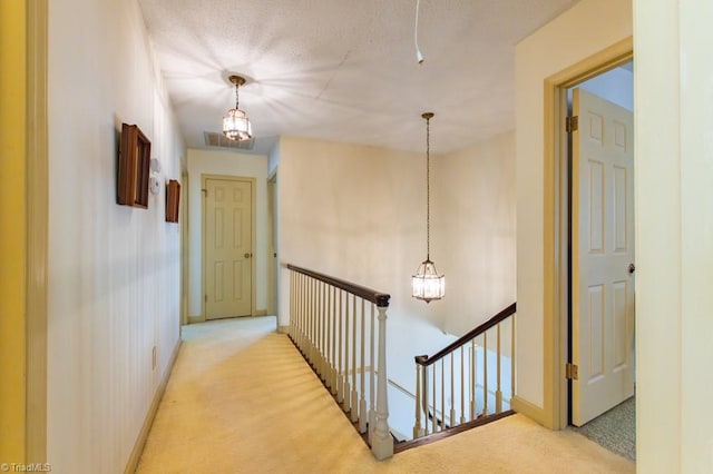 hallway with an upstairs landing, light carpet, a textured ceiling, baseboards, and a chandelier