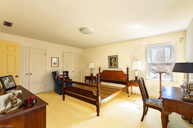 bedroom featuring visible vents, multiple closets, light colored carpet, and a textured ceiling