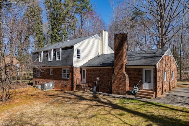 rear view of house with a lawn, entry steps, crawl space, brick siding, and a chimney