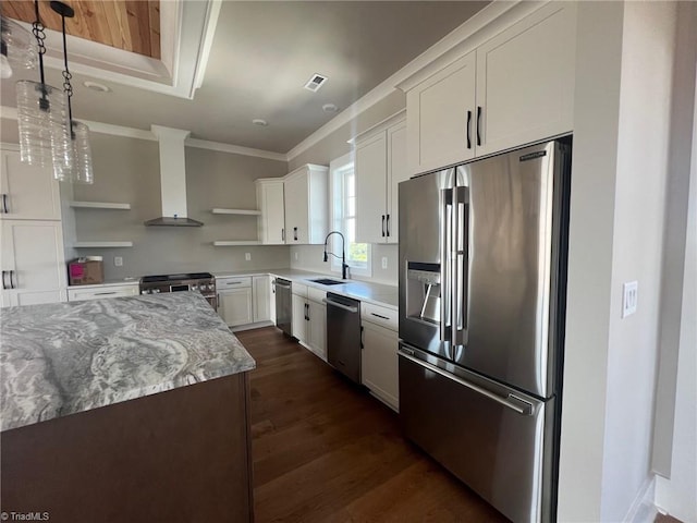 kitchen with appliances with stainless steel finishes, white cabinets, wall chimney exhaust hood, pendant lighting, and crown molding