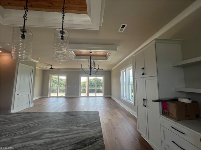 unfurnished dining area featuring a raised ceiling, ornamental molding, hardwood / wood-style floors, and ceiling fan