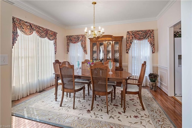 dining area with a healthy amount of sunlight, hardwood / wood-style floors, ornamental molding, and a chandelier