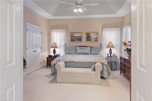 bedroom featuring light colored carpet, a raised ceiling, and a closet