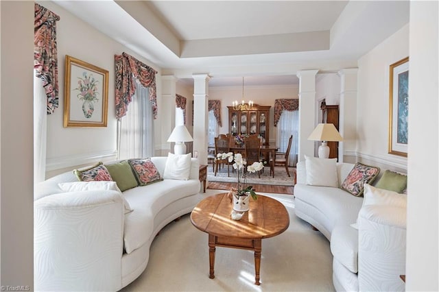 living room featuring a notable chandelier, decorative columns, and a raised ceiling