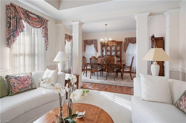 living room with hardwood / wood-style flooring, crown molding, a chandelier, and decorative columns