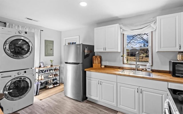 laundry area with light hardwood / wood-style floors, stacked washer and dryer, sink, and electric panel