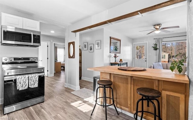 kitchen featuring a breakfast bar, wooden counters, ceiling fan, appliances with stainless steel finishes, and white cabinetry