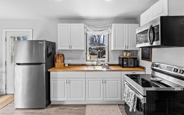 kitchen featuring wooden counters, appliances with stainless steel finishes, white cabinetry, and sink