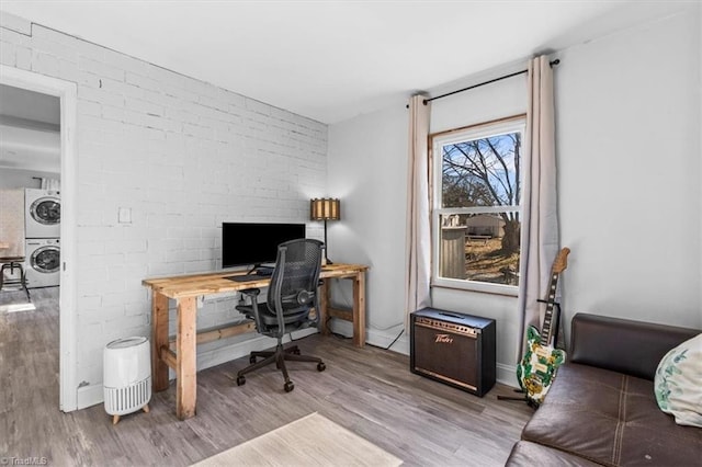 office area featuring light hardwood / wood-style floors, brick wall, and stacked washer and clothes dryer