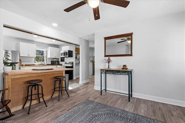 kitchen with kitchen peninsula, appliances with stainless steel finishes, a breakfast bar, wood-type flooring, and white cabinets