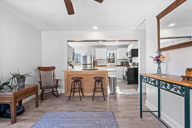 kitchen with white cabinetry, ceiling fan, wood-type flooring, a breakfast bar area, and appliances with stainless steel finishes