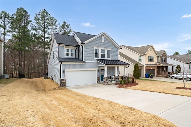 view of front of property featuring a porch, a garage, driveway, stone siding, and a standing seam roof