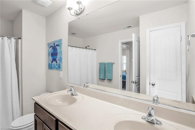 full bathroom with toilet, double vanity, visible vents, and a sink