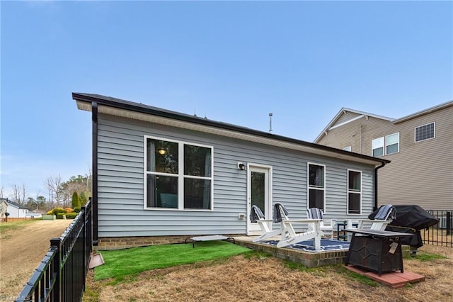 rear view of property with an outdoor fire pit, fence, and a lawn