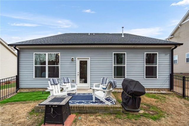 rear view of house featuring a yard, a fenced backyard, an outdoor fire pit, and roof with shingles