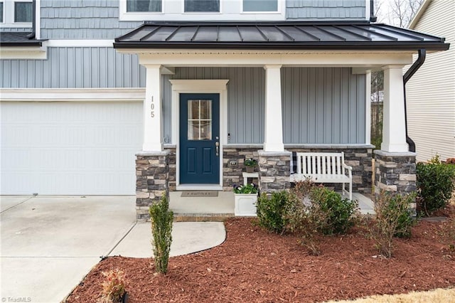 entrance to property featuring metal roof, a porch, a garage, stone siding, and a standing seam roof