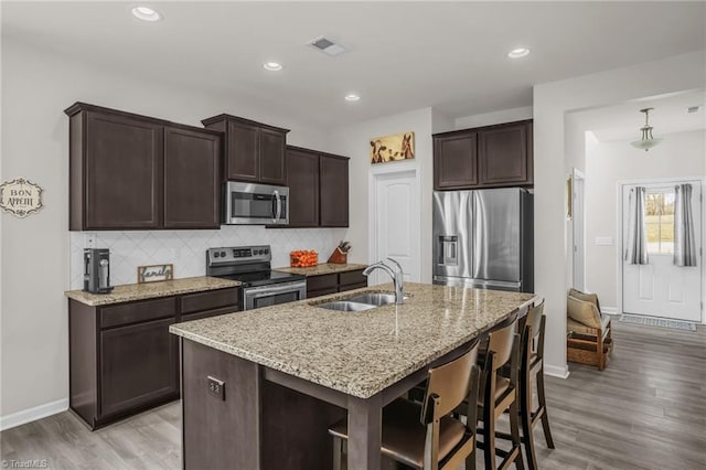 kitchen with dark brown cabinetry, stainless steel appliances, a sink, visible vents, and backsplash