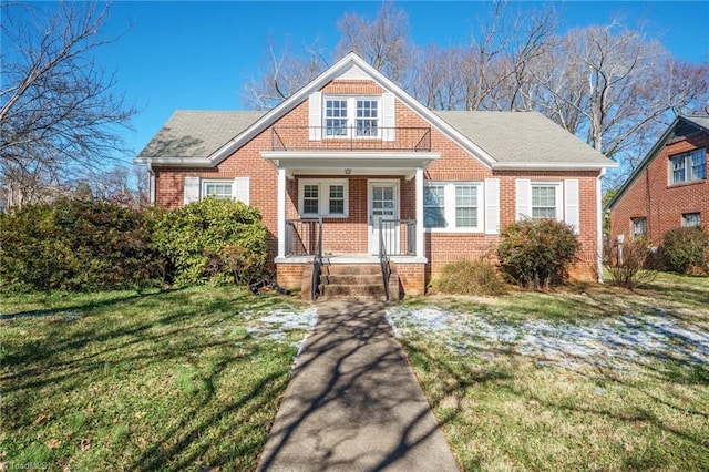 view of front of property with roof with shingles, a front lawn, a porch, and brick siding