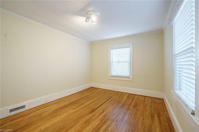 unfurnished room featuring light wood finished floors, baseboards, visible vents, and crown molding