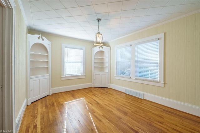 unfurnished dining area featuring crown molding, wood finished floors, visible vents, and built in features