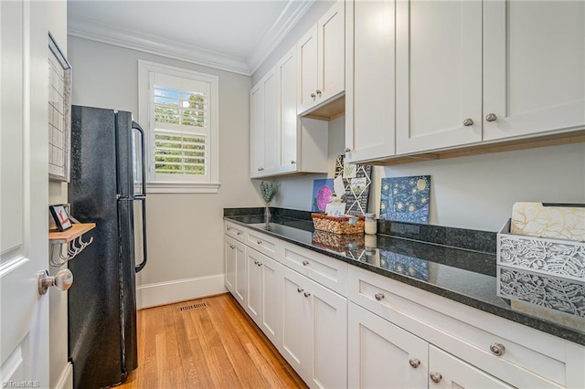 kitchen featuring dark stone counters, light wood-style flooring, freestanding refrigerator, ornamental molding, and white cabinetry