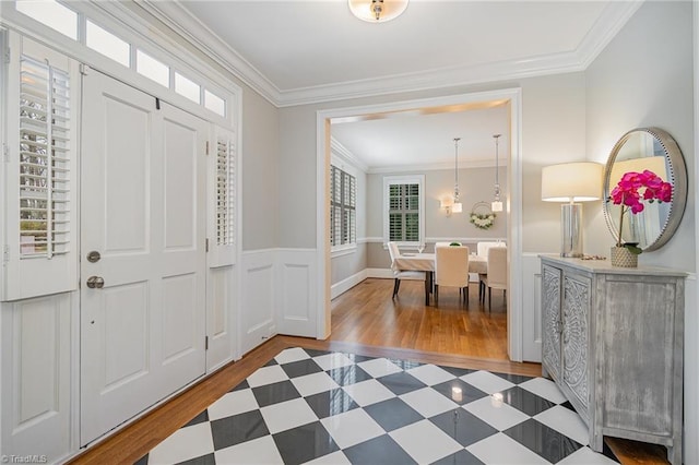 entryway with wood finished floors, a healthy amount of sunlight, wainscoting, and crown molding