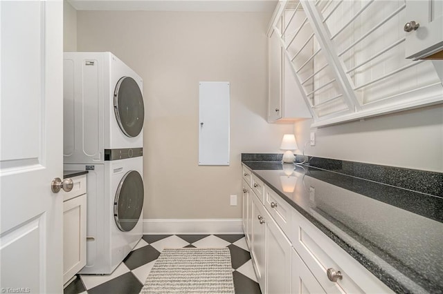 laundry room with tile patterned floors, baseboards, cabinet space, and stacked washer and dryer