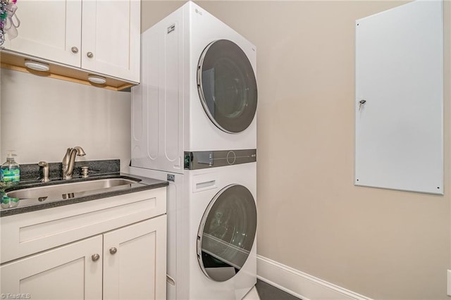 laundry area featuring stacked washer / dryer, cabinet space, baseboards, and a sink