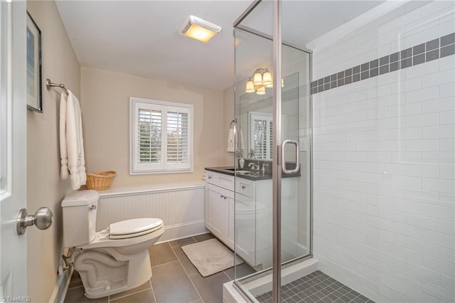 bathroom with tile patterned floors, a wainscoted wall, a stall shower, and toilet